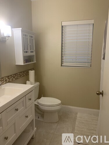 A bathroom with a toilet, sink, and a window with blinds.