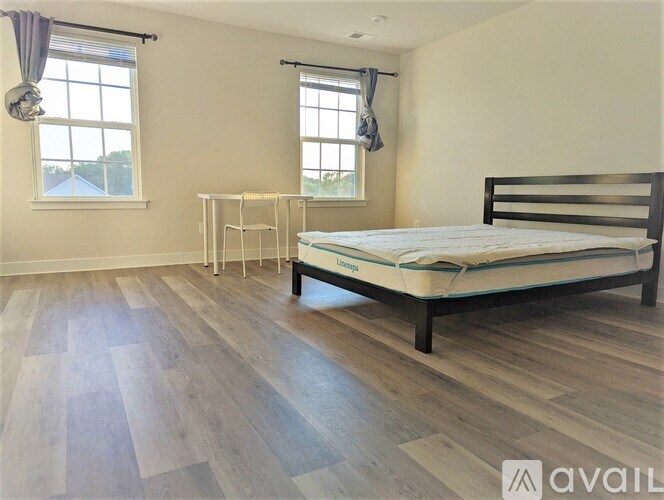 A bedroom with a bed, a small table, and two windows.