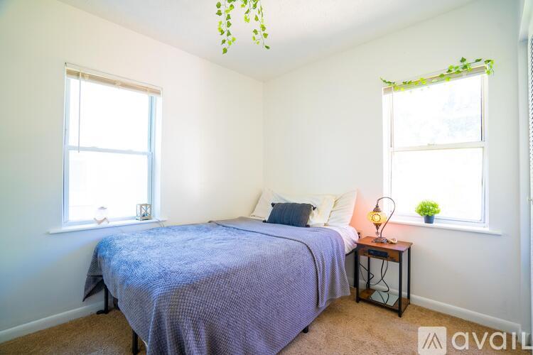 A bedroom with a bed, a window with a plant on it, and a lamp on a side table.