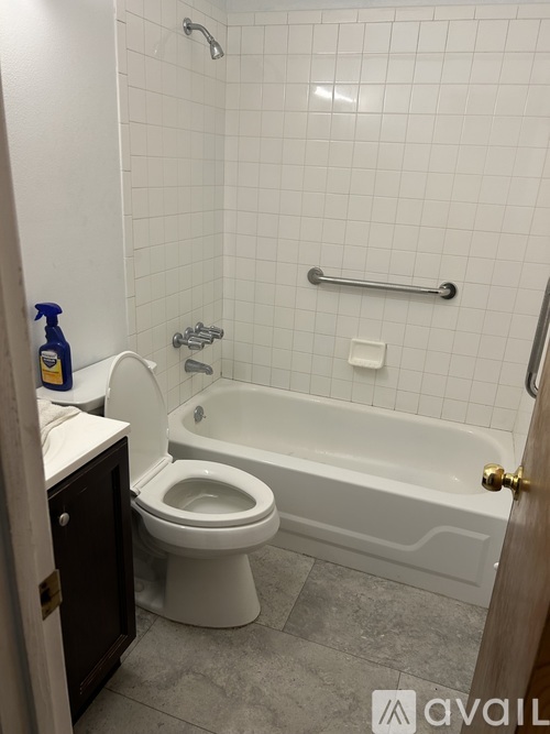 A white tiled bathroom with a toilet, tub, and toilet paper.