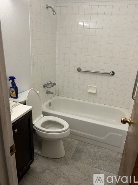 A white tiled bathroom with a toilet, tub, and toilet paper.
