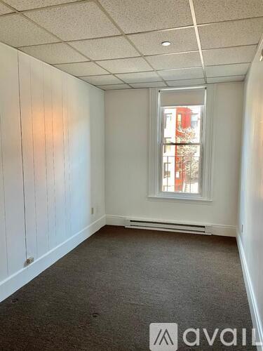 A room with white walls and a window with a view of a red building outside.