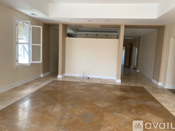 A large empty room with tiled flooring and a window on the left side.