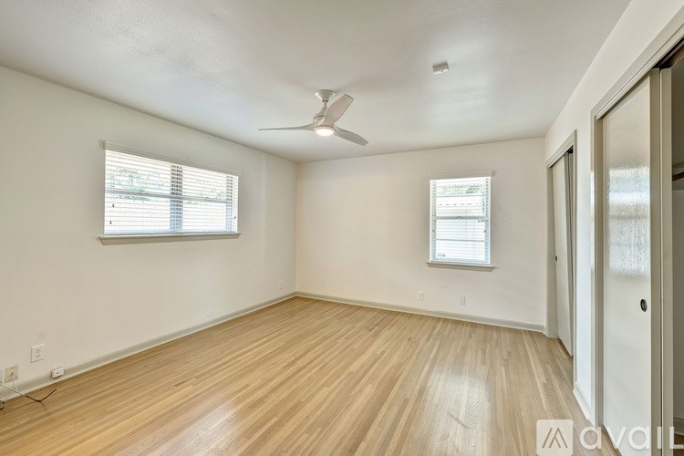 A room with wooden flooring and two windows.