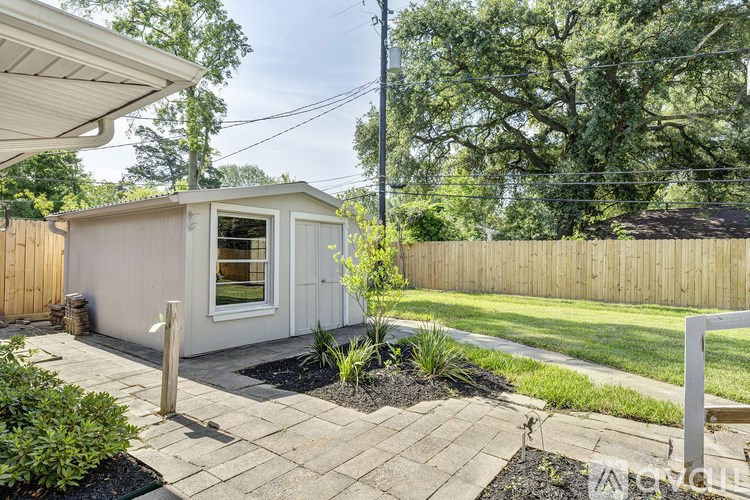 A small white shed with a window and a door is surrounded by a wooden fence and a small garden.