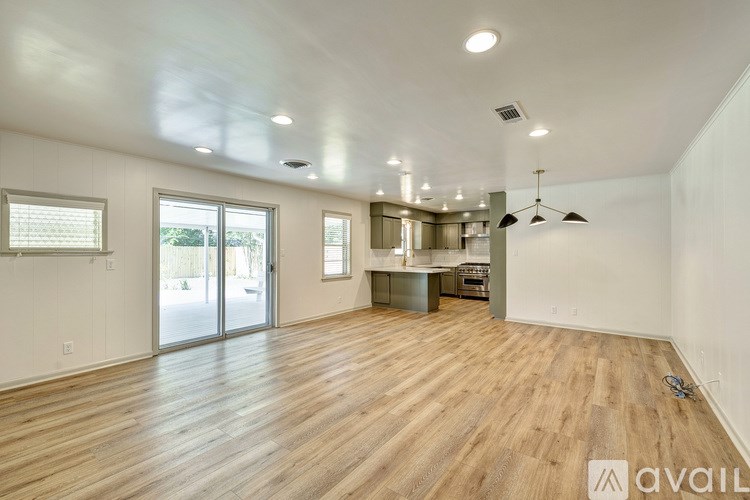 A spacious room with wooden flooring and a kitchen area in the background.