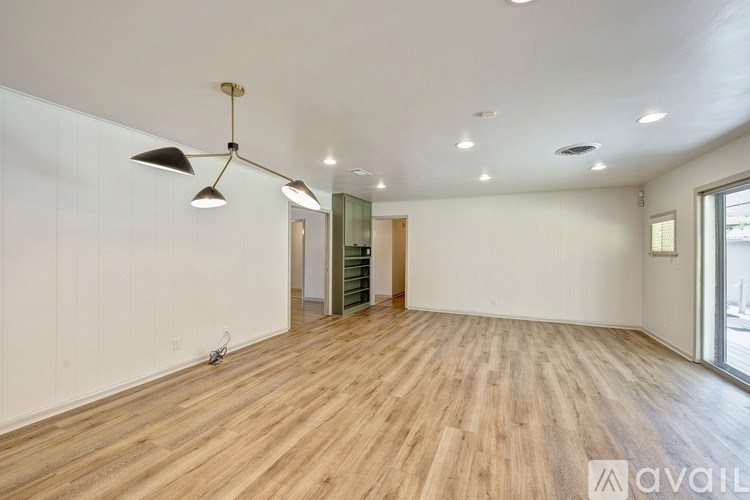 A spacious room with wooden flooring and a large window on the right side.