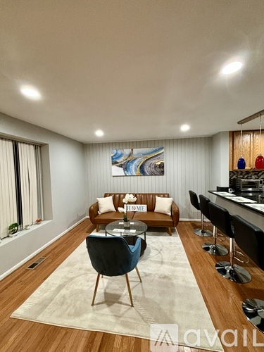 A living room with a blue chair in the center and a painting on the wall.