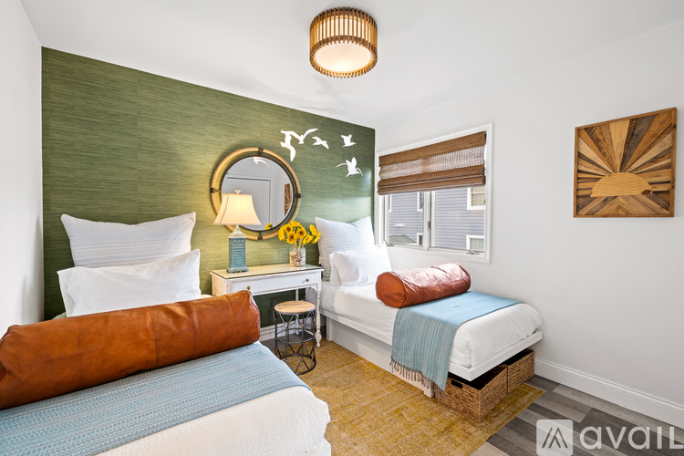 A bedroom with two beds, one with a blue blanket, and a desk with a lamp and a vase of flowers.