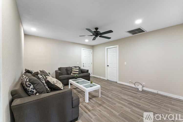 A living room with a grey couch, a glass coffee table, and a ceiling fan.