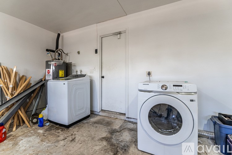 A white washing machine sits in a room with a door and a wall heater.