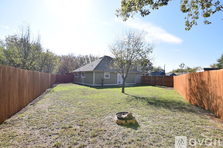 A backyard with a fence, a tree, and a house in the background.