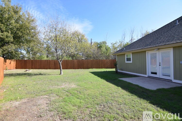 A backyard with a fence, a tree, and a house.
