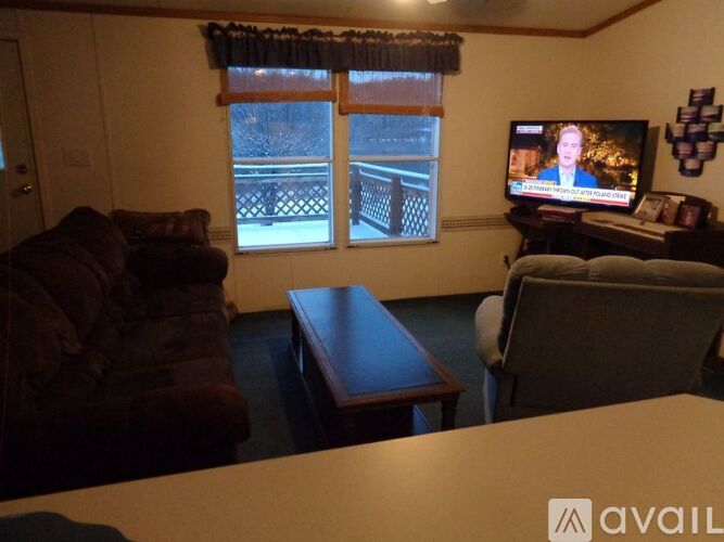 A living room with a brown couch, a wooden coffee table, and a television displaying a news program.