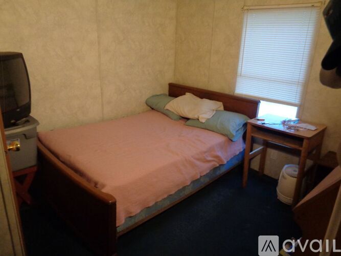 A bedroom with a bed, nightstand, and a window with blinds.