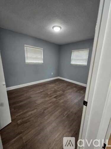 A room with wooden flooring and two windows with blinds.
