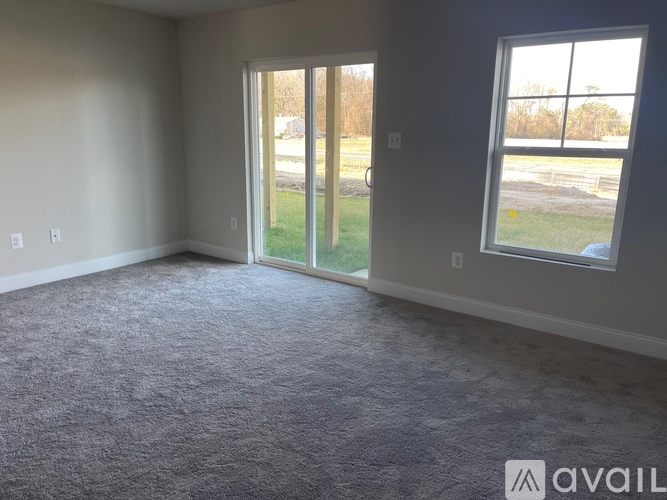 A room with grey carpet and a large window overlooking a field.