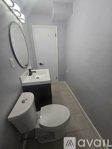 A bathroom with a toilet, sink, mirror and light.