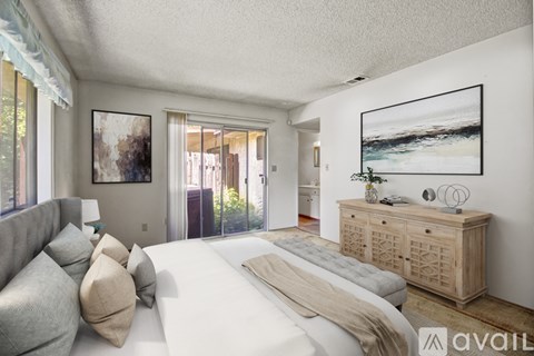 A bedroom with a large bed, a grey sofa, and a wooden cabinet.