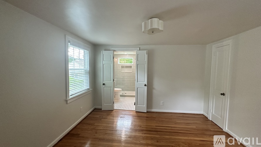 A room with wooden floors and white walls, with a doorway leading to another room.