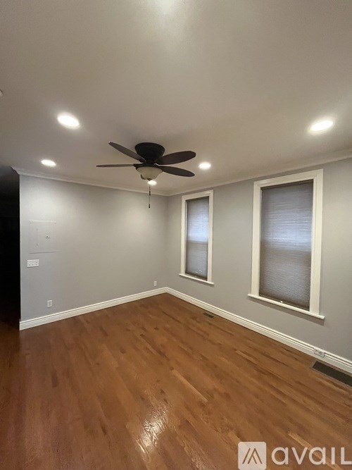 A room with a ceiling fan and two windows.