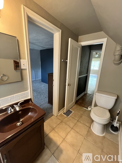 A bathroom with a toilet, sink, and a door leading to a bedroom.