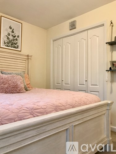 A bedroom with a pink bedspread and a white wardrobe.