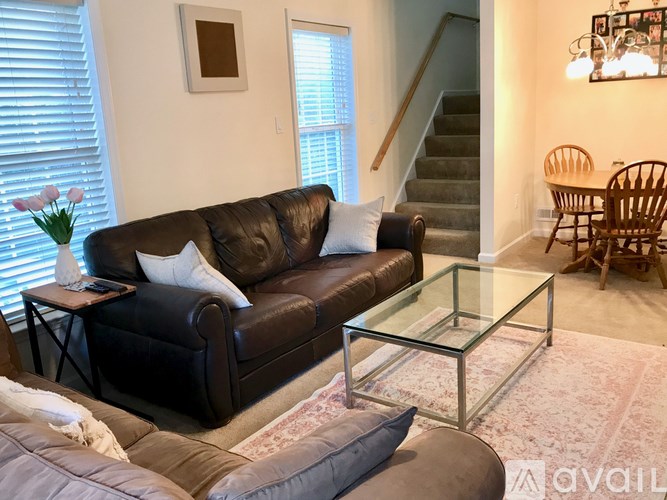 A living room with a brown couch, glass coffee table, and a staircase in the background.