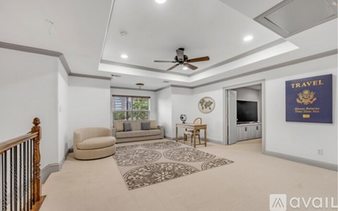 A living room with a beige carpet and a ceiling fan.