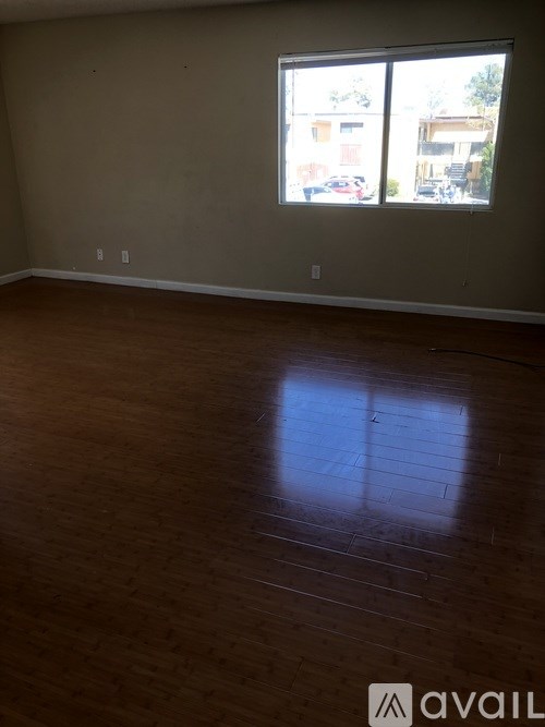 A room with wooden flooring and a window showing a view of a street.