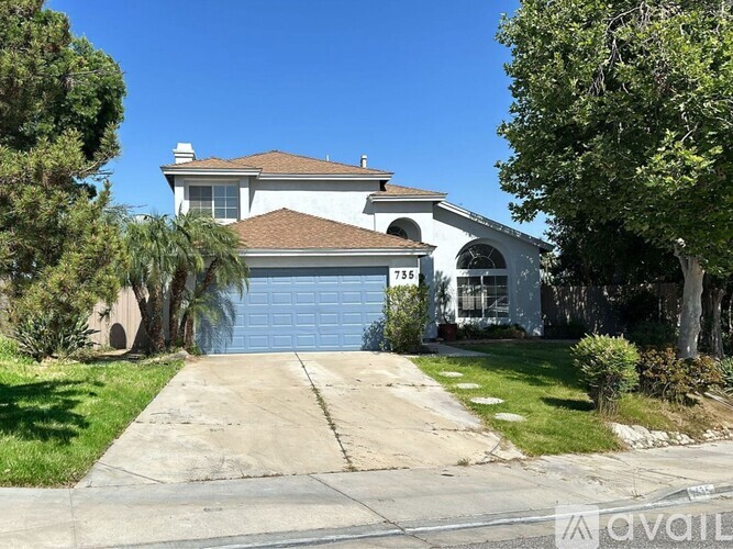 A house with a blue garage door is surrounded by trees.