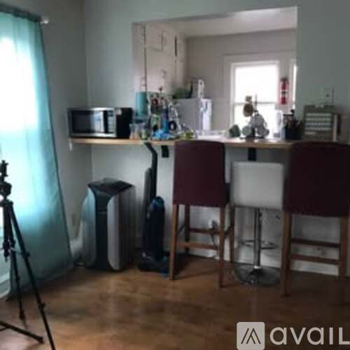 A kitchen with a microwave, a fridge, a stove, a dining table with chairs and a tripod.