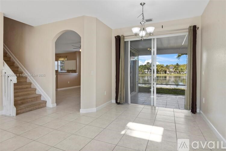 A spacious living room with a staircase and a view of the outdoors through a sliding glass door.