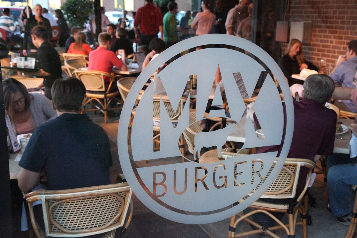 people sitting at an outdoor restaurant with a may burger sign