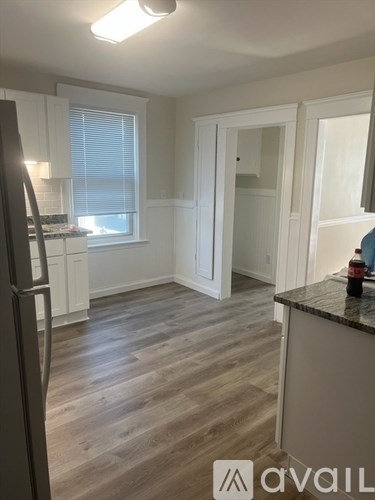 A kitchen with a refrigerator on the left and a counter with a bottle on it.