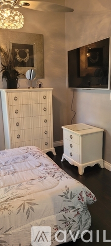A white chest of drawers sits next to a white bed in a room.