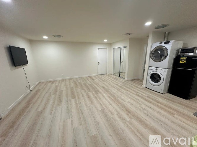 A room with a wooden floor and a washing machine on top of a dryer.
