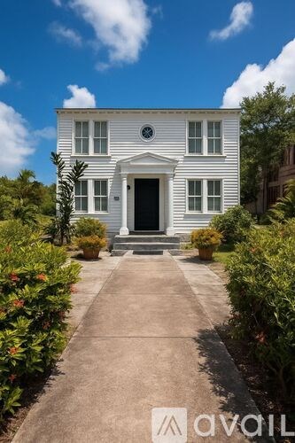 A white house with a black door and windows surrounded by greenery.