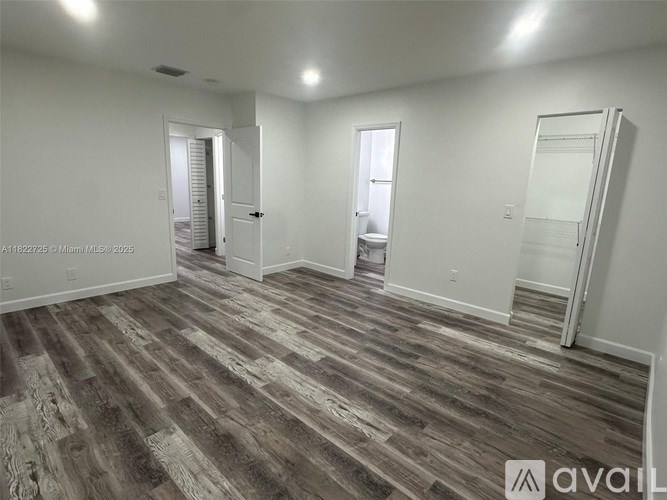 A room with wooden flooring and white walls, with a door on the left and a closet on the right.