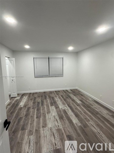 A room with wooden flooring and a window with blinds.