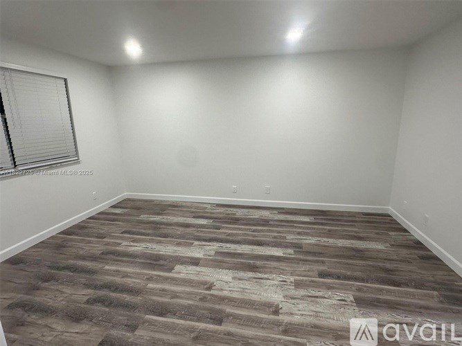 A room with a wooden floor and a window with blinds.