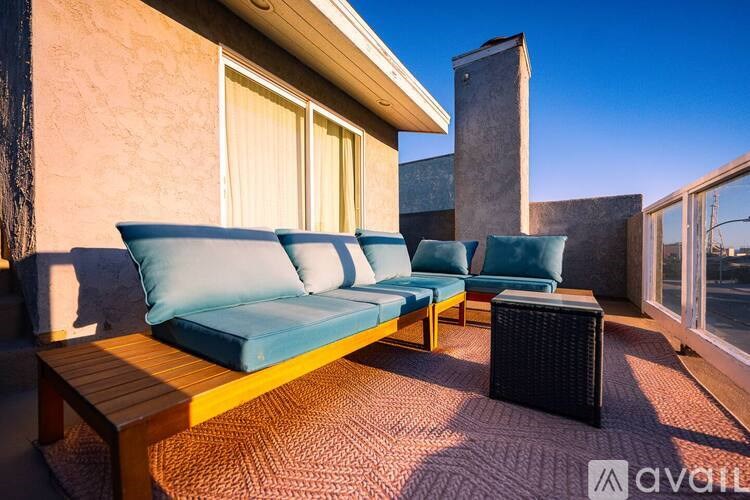 A blue couch is on a wooden deck with a table and a black ottoman.