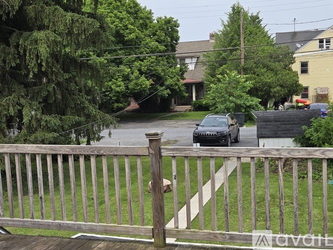A black car is parked on a street behind a wooden fence.