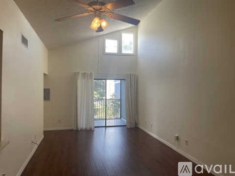 A spacious room with a ceiling fan and sliding glass doors leading to a balcony.