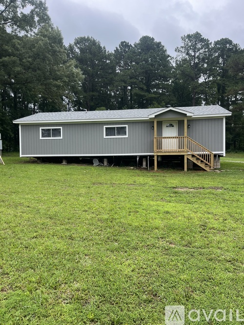 A grey house with a porch and a white door is surrounded by green grass.