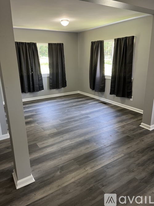 A room with grey wooden flooring and black curtains.