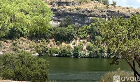 A body of water surrounded by greenery and a rocky cliff.