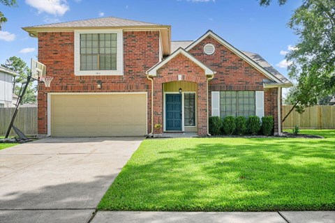 A red brick house with a garage door and a green lawn.