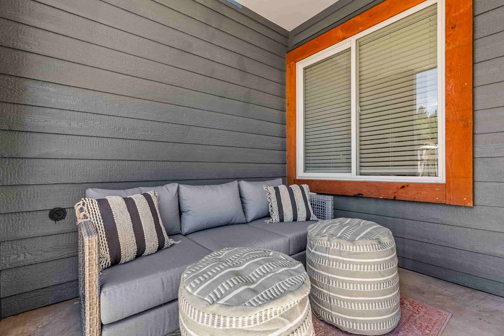 A grey couch with striped pillows sits on a patio with two round ottomans.