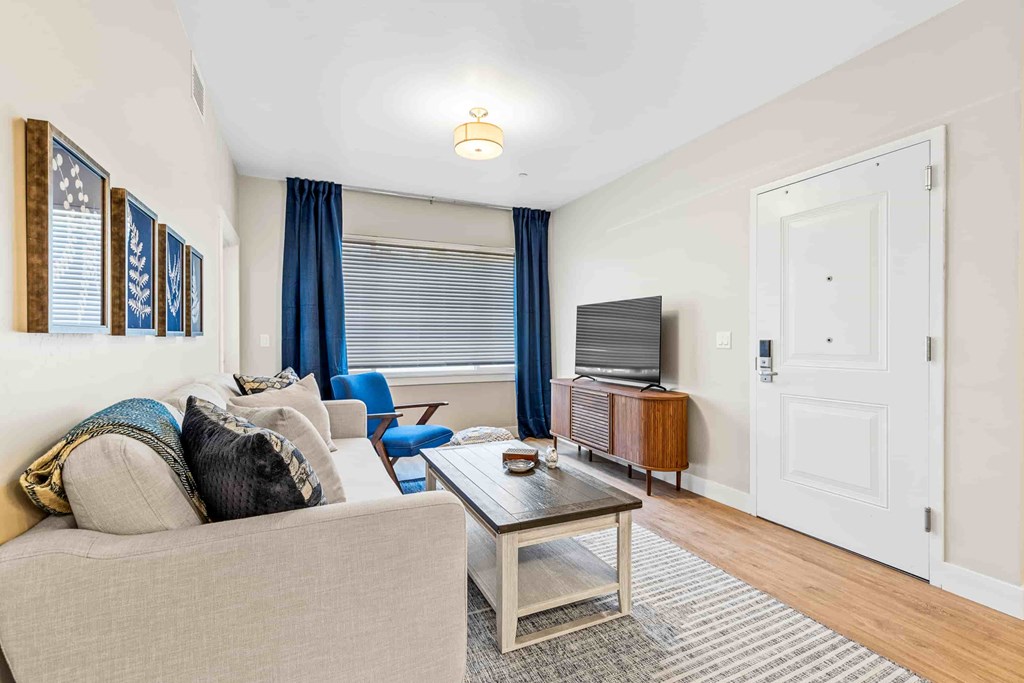 A living room with a grey couch, a blue chair, a wooden coffee table, and a white door.